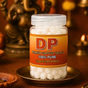 Jar of DP premium camphor tablets (100 g) on a brass plate, set against a warm, worship-themed background with a statue.